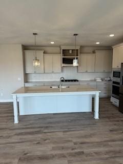 kitchen with pendant lighting, oven, dark hardwood / wood-style flooring, and a center island with sink