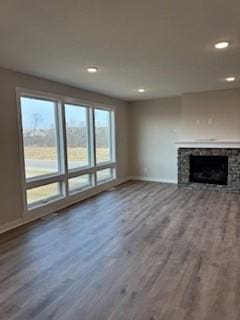 unfurnished living room with hardwood / wood-style flooring and a stone fireplace