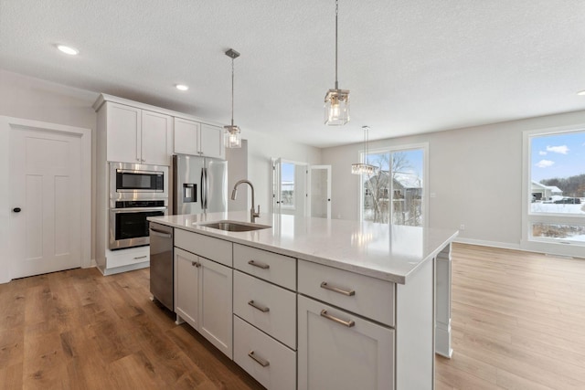 kitchen featuring appliances with stainless steel finishes, pendant lighting, sink, a kitchen island with sink, and light stone counters