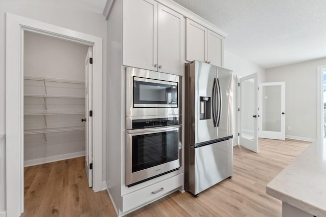 kitchen featuring a textured ceiling, light hardwood / wood-style flooring, stainless steel appliances, and white cabinets