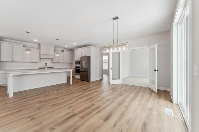 kitchen with pendant lighting, appliances with stainless steel finishes, backsplash, a kitchen breakfast bar, and an island with sink