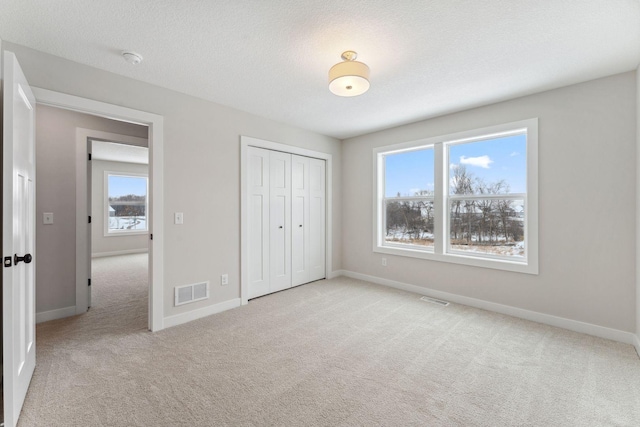 unfurnished bedroom with light carpet, a textured ceiling, and a closet