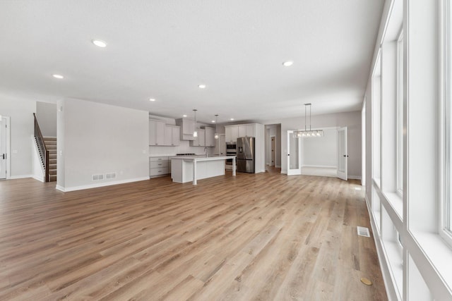 unfurnished living room featuring sink, a chandelier, and light hardwood / wood-style floors