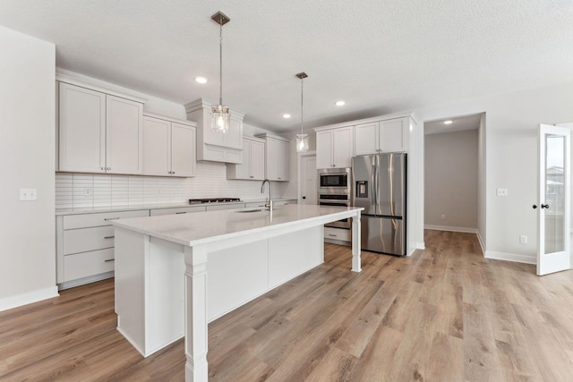 kitchen featuring sink, appliances with stainless steel finishes, a kitchen island with sink, white cabinetry, and decorative light fixtures