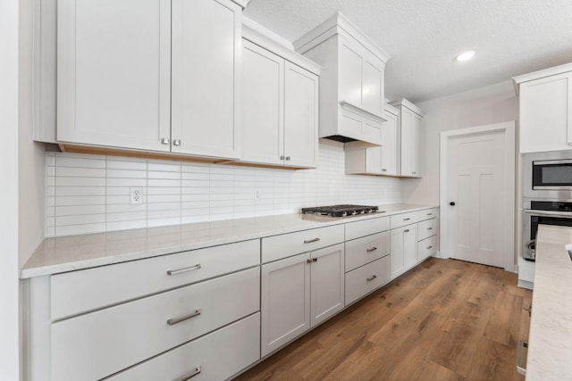 kitchen with white cabinetry, stainless steel appliances, tasteful backsplash, wood-type flooring, and light stone countertops