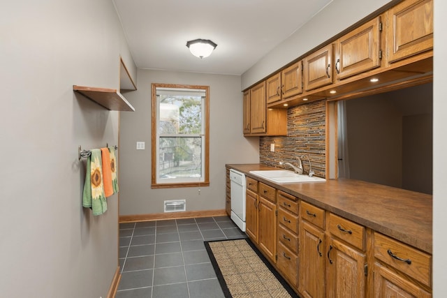 kitchen with decorative backsplash, white dishwasher, dark tile patterned floors, and sink