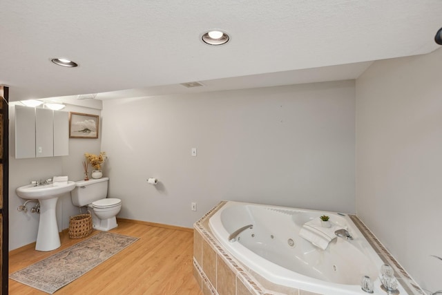 bathroom featuring tiled bath, toilet, wood-type flooring, and sink