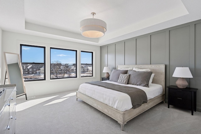 bedroom with light carpet, a tray ceiling, and a decorative wall