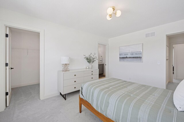 bedroom with light carpet, baseboards, visible vents, a walk in closet, and a closet