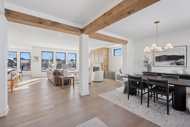 dining space with a glass covered fireplace, beamed ceiling, an inviting chandelier, light wood-type flooring, and recessed lighting