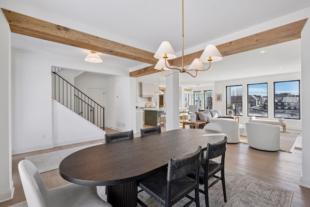 dining space with a chandelier, wood finished floors, baseboards, stairway, and beamed ceiling