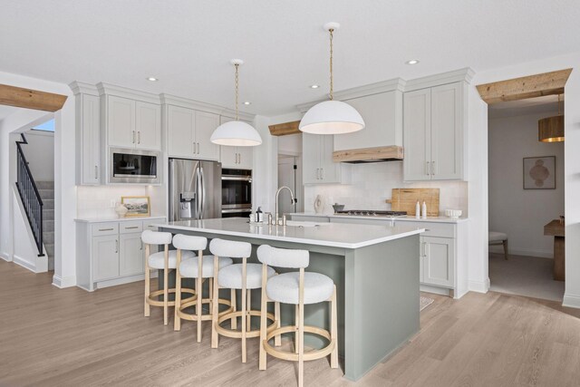 kitchen with a breakfast bar area, stainless steel appliances, light countertops, a sink, and an island with sink