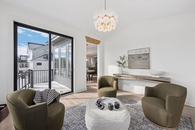 living area featuring a notable chandelier, wood finished floors, visible vents, baseboards, and vaulted ceiling