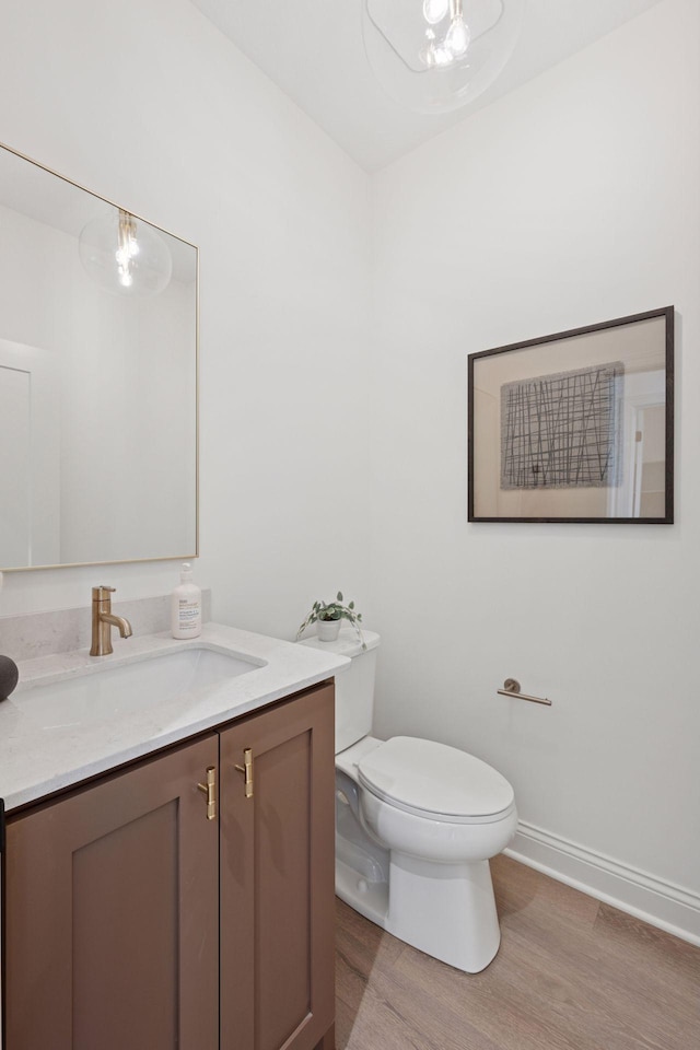 half bathroom featuring toilet, baseboards, wood finished floors, and vanity