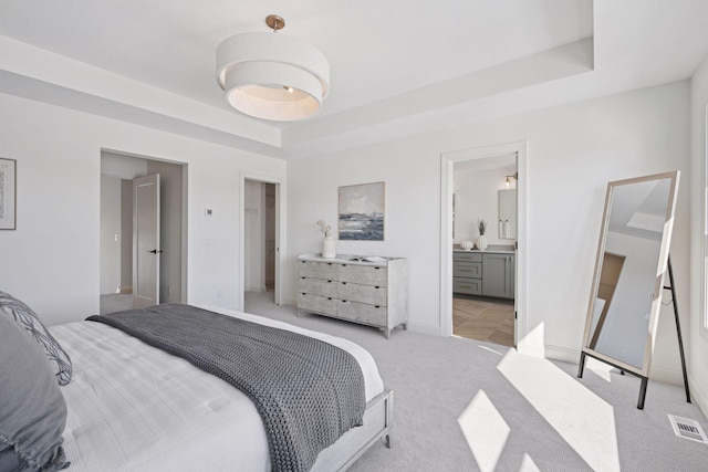 bedroom with visible vents, a raised ceiling, connected bathroom, and light colored carpet