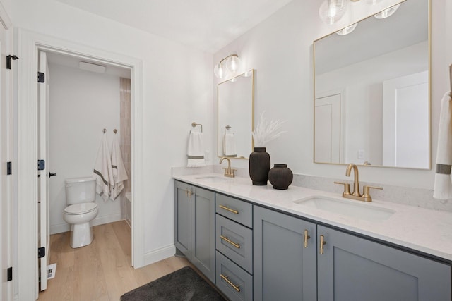 full bathroom with toilet, double vanity, a sink, and wood finished floors