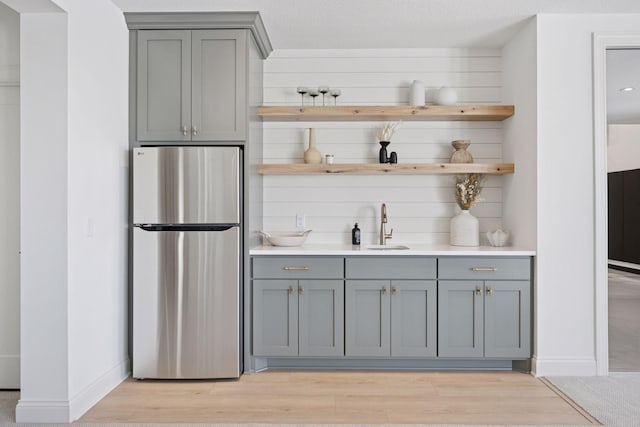 bar with light wood-style floors, freestanding refrigerator, a sink, and baseboards