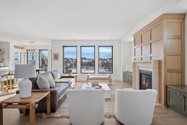 living area with light wood-style flooring, a chandelier, and a glass covered fireplace