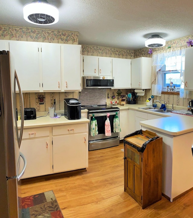 kitchen featuring white cabinetry, sink, stainless steel appliances, light hardwood / wood-style flooring, and a textured ceiling