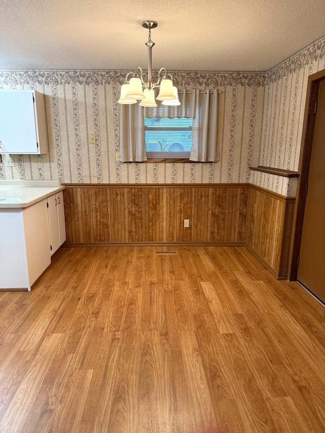 2402 Kenwood Dr SW, Willmar, MN 56201 - unfurnished dining area featuring light wood-style flooring, a wainscoted wall, a chandelier, wallpapered walls, and a textured ceiling