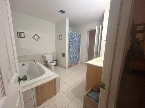 bathroom featuring tile patterned flooring, vanity, toilet, and tiled tub