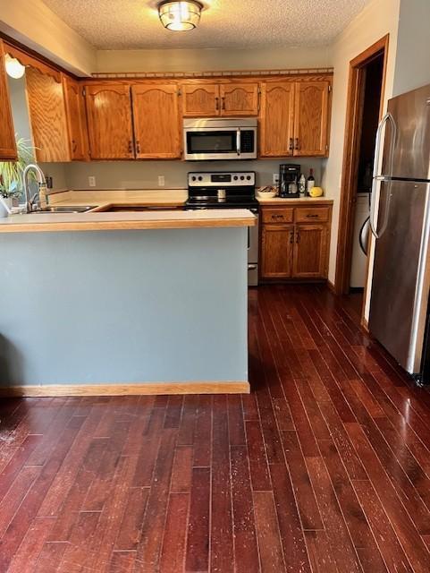 kitchen with dark wood-type flooring, sink, kitchen peninsula, and stainless steel appliances