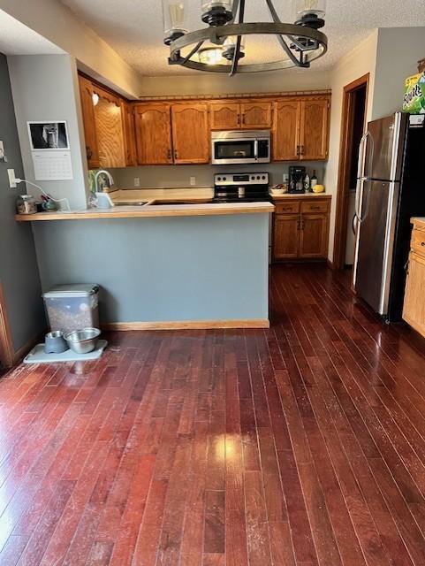 kitchen featuring kitchen peninsula, sink, dark wood-type flooring, appliances with stainless steel finishes, and a textured ceiling