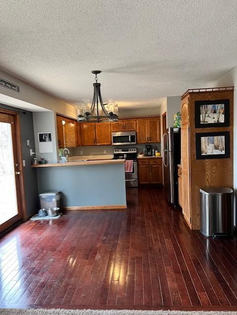 kitchen featuring kitchen peninsula, stainless steel appliances, dark hardwood / wood-style floors, a notable chandelier, and decorative light fixtures