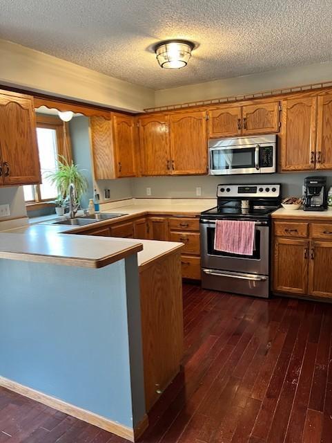 kitchen featuring kitchen peninsula, appliances with stainless steel finishes, dark hardwood / wood-style flooring, and a textured ceiling