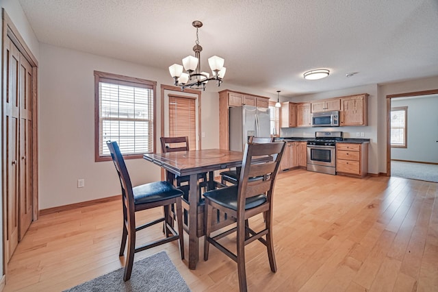 dining area featuring a textured ceiling, an inviting chandelier, light wood-type flooring, and a healthy amount of sunlight