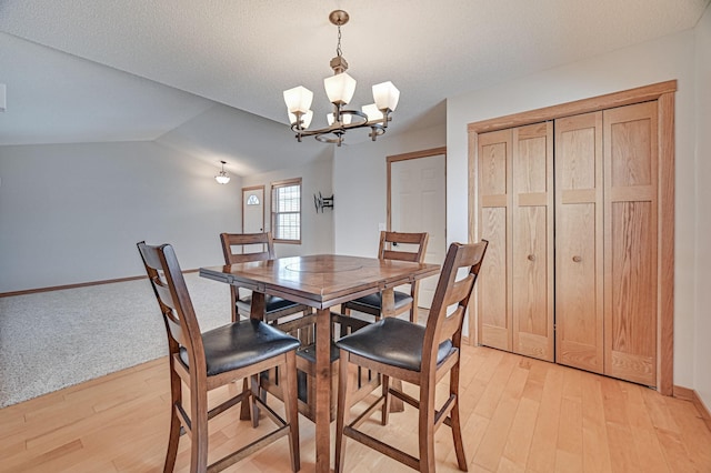 dining area with lofted ceiling, an inviting chandelier, light hardwood / wood-style floors, and a textured ceiling