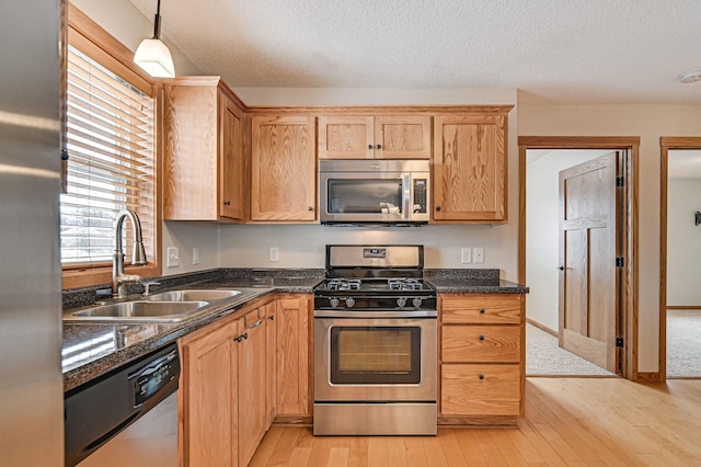 kitchen featuring appliances with stainless steel finishes, light hardwood / wood-style floors, a textured ceiling, decorative light fixtures, and sink