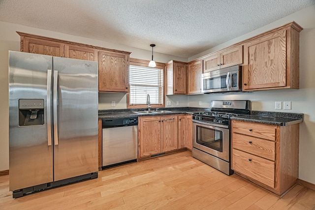 kitchen featuring appliances with stainless steel finishes, light wood-type flooring, a textured ceiling, decorative light fixtures, and sink