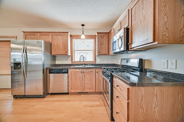 kitchen with sink, a textured ceiling, light hardwood / wood-style flooring, pendant lighting, and appliances with stainless steel finishes