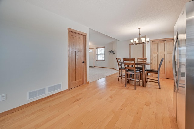 dining space with a textured ceiling, a chandelier, and light hardwood / wood-style flooring