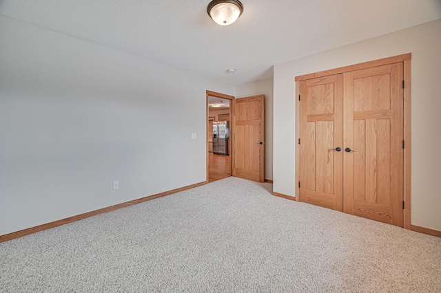 unfurnished bedroom with a closet, light carpet, and stainless steel refrigerator with ice dispenser