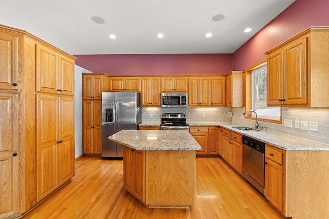 kitchen with light hardwood / wood-style floors, appliances with stainless steel finishes, sink, a kitchen island, and light stone counters