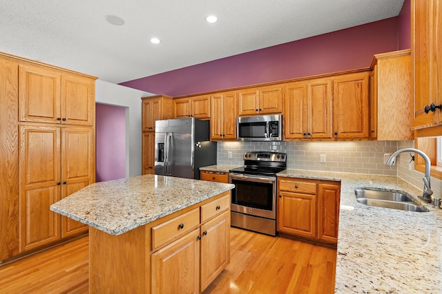 kitchen featuring a kitchen island, stainless steel appliances, tasteful backsplash, sink, and light stone counters