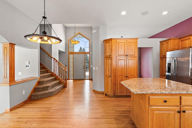 kitchen with stainless steel fridge with ice dispenser, a center island, hanging light fixtures, and light stone counters