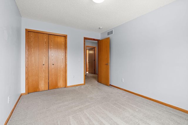 unfurnished bedroom featuring a textured ceiling, light colored carpet, and a closet