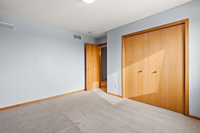 unfurnished bedroom featuring light colored carpet, a textured ceiling, and a closet