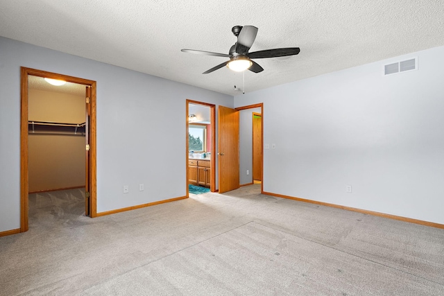 unfurnished bedroom with a walk in closet, connected bathroom, light carpet, a closet, and ceiling fan