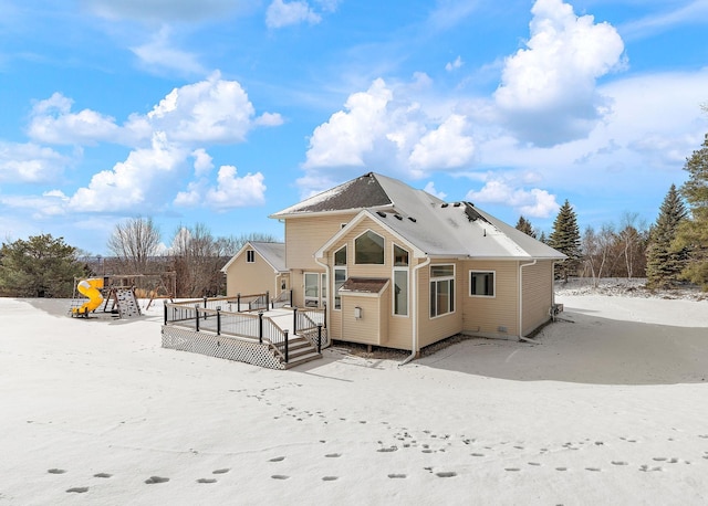 snow covered back of property with a playground and a wooden deck