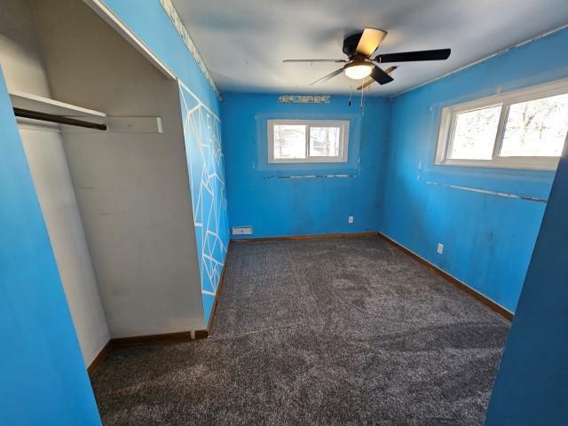 unfurnished bedroom featuring multiple windows, ceiling fan, and dark carpet