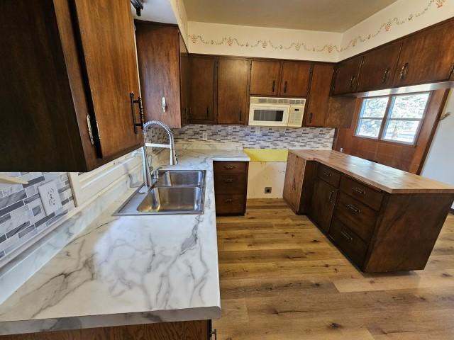 kitchen with light wood-type flooring, dark brown cabinets, backsplash, and sink