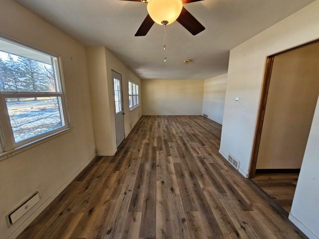 unfurnished room with a healthy amount of sunlight, ceiling fan, and dark wood-type flooring