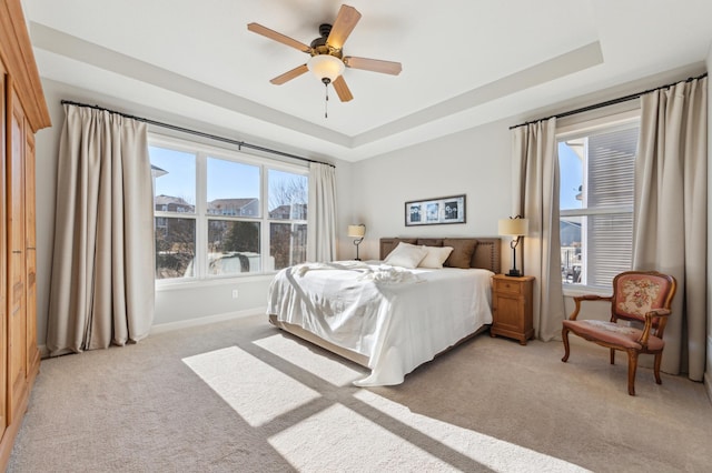 bedroom with a ceiling fan, a raised ceiling, light carpet, and baseboards