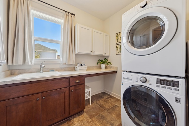 laundry area with stone finish floor, stacked washing maching and dryer, baseboards, and a sink