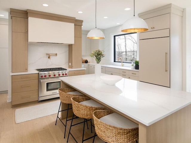 kitchen with tasteful backsplash, hanging light fixtures, light wood-style flooring, premium range, and a kitchen breakfast bar