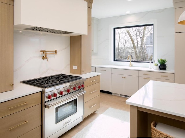 kitchen featuring luxury stove, a sink, custom exhaust hood, light stone countertops, and tasteful backsplash